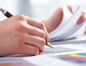 Close up of a persons hand holding a pen, making notes on some documents